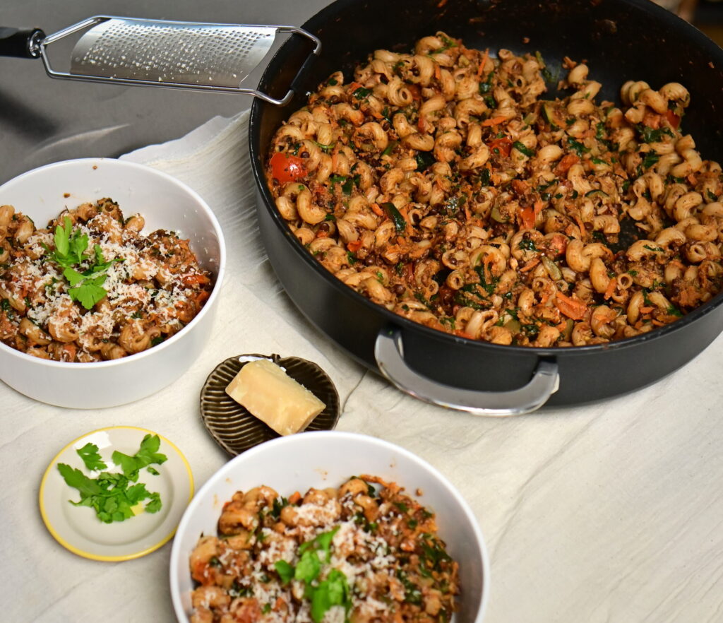 Two bowls and a pot of lentil and mushroom ragù with curly pasta.