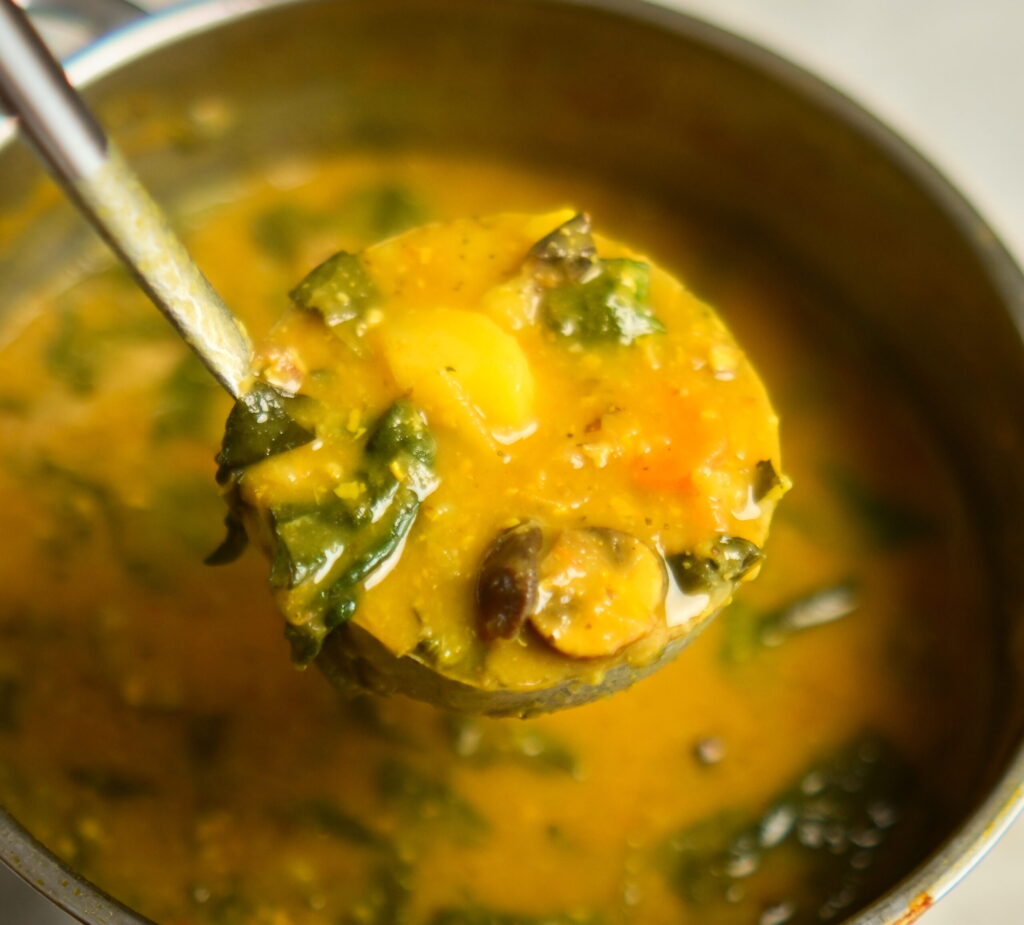Lemony chickpea and vegetable soup with a ladle above a pot of soup.