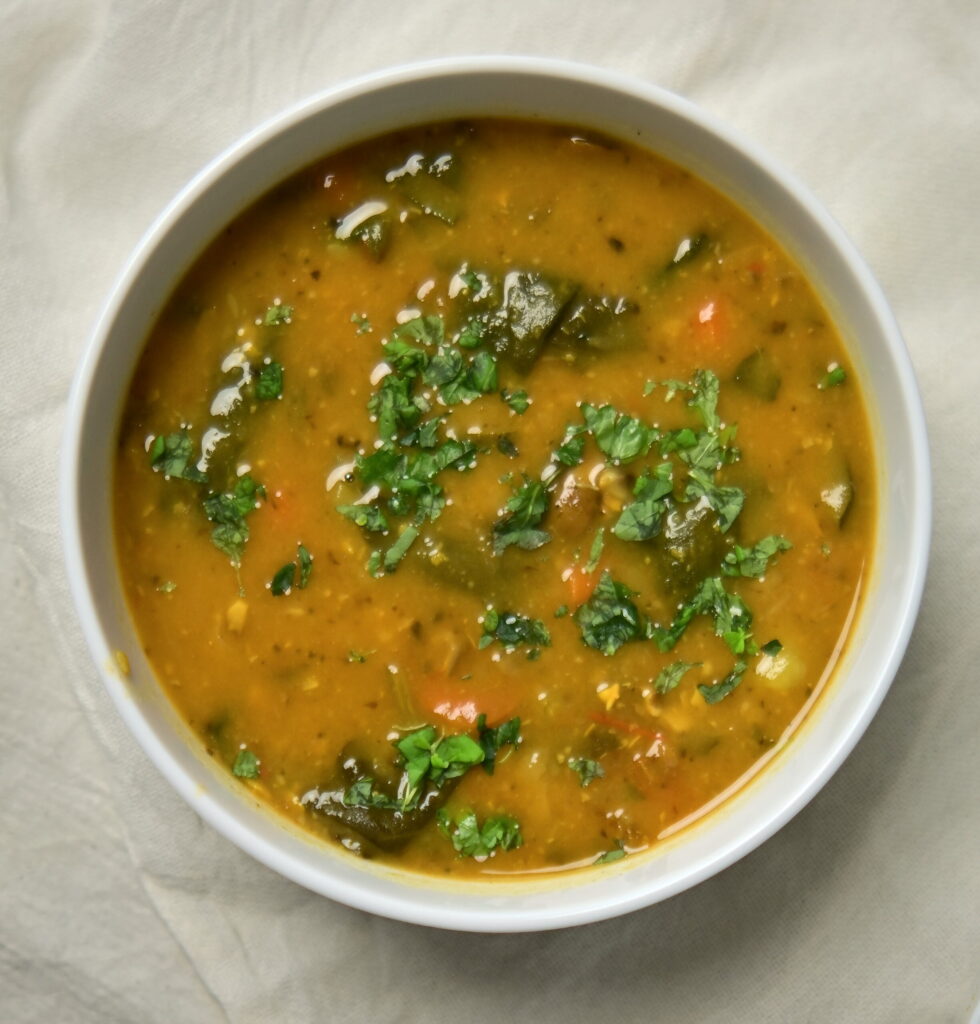 A white bowl of lemony chickpea and vegetable soup with chopped parsley on top.