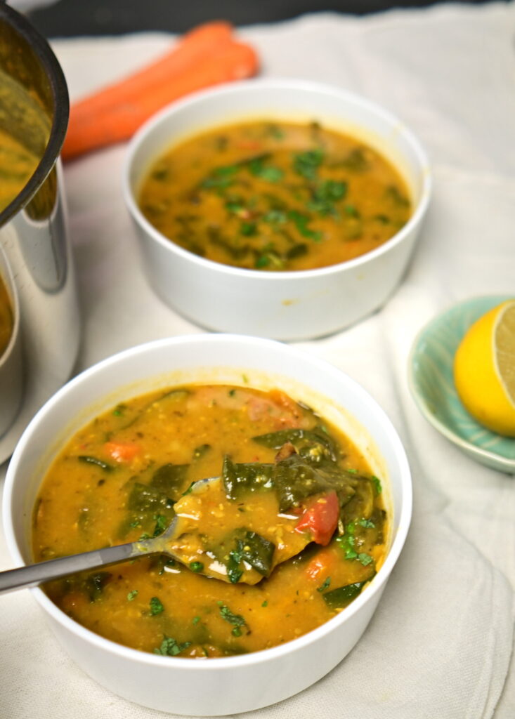 Two bowls of lemony chickpea and vegetable soup with a pot, lemon, and carrot.