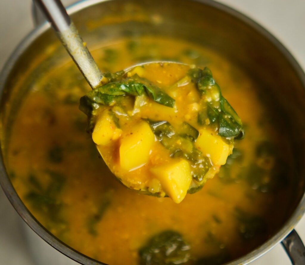 Lemony chickpea and vegetable soup with a ladle above a pot of soup.