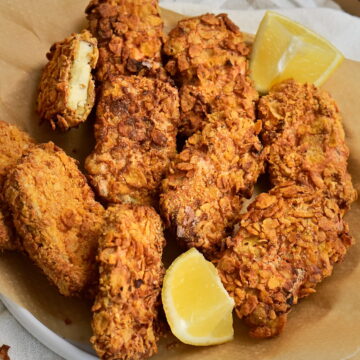 A bowl lined with parchment paper, filled with tofu nuggets and lemon wedges.