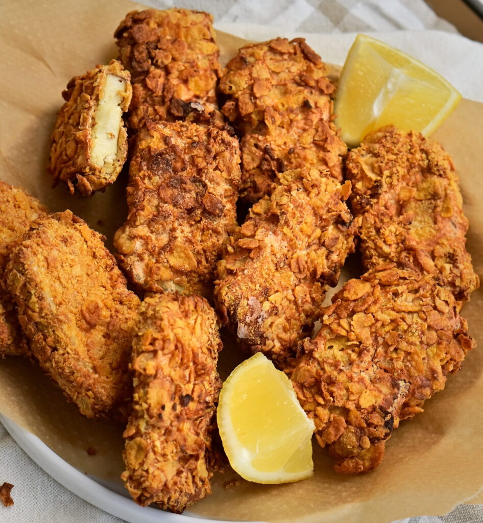 A bowl lined with parchment paper, filled with tofu nuggets and lemon wedges.