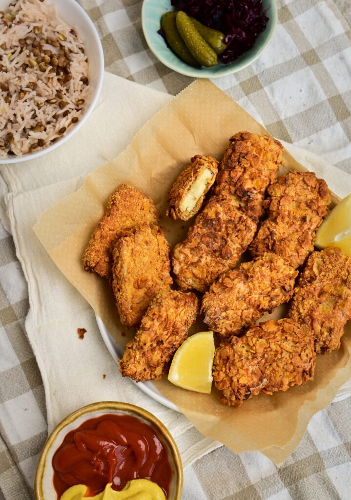 bowl filled with tofu nuggets and lemon wedges On a tablecloth, with dips and cabbage.