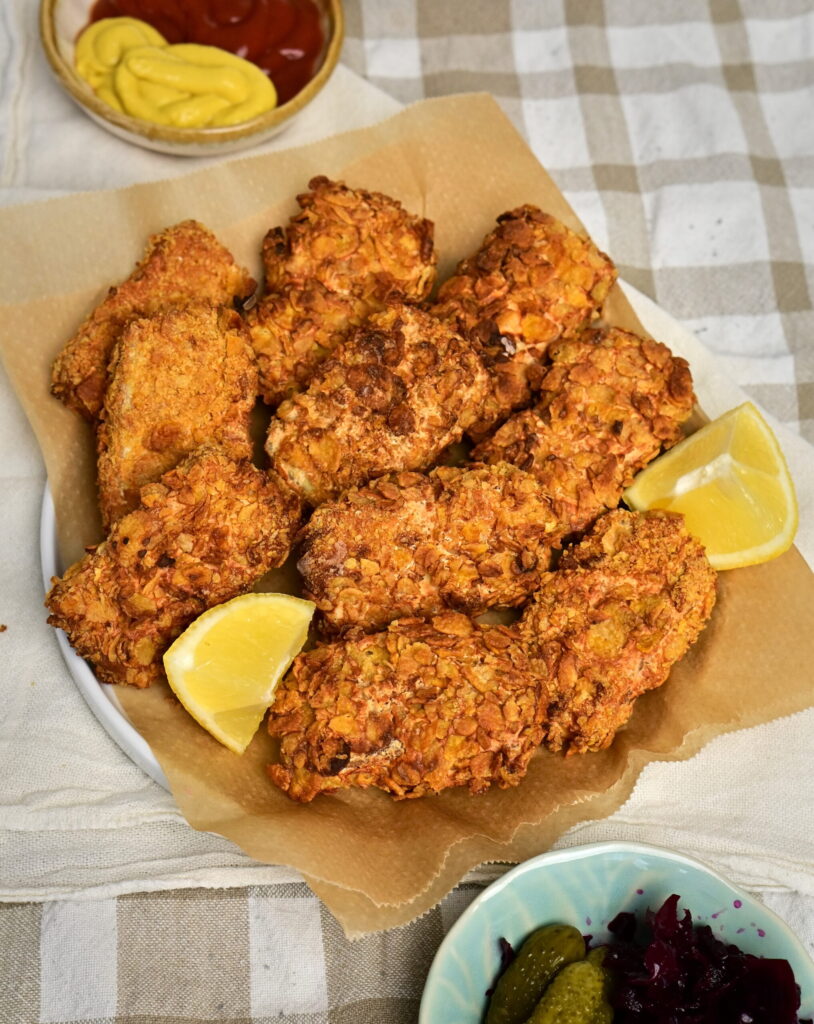 bowl filled with tofu nuggets and lemon wedges On a tablecloth, with dips and cabbage.