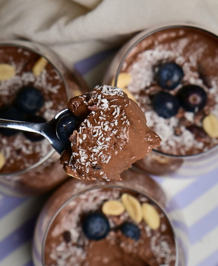 A spoon with chocolate mousse above decorated serving glasses.