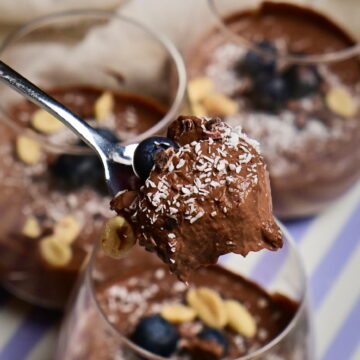 A spoon with chocolate mousse above decorated serving glasses.