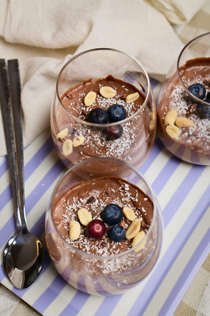 Chocolate mousse in serving glasses with coconut, peanuts, and blueberries.