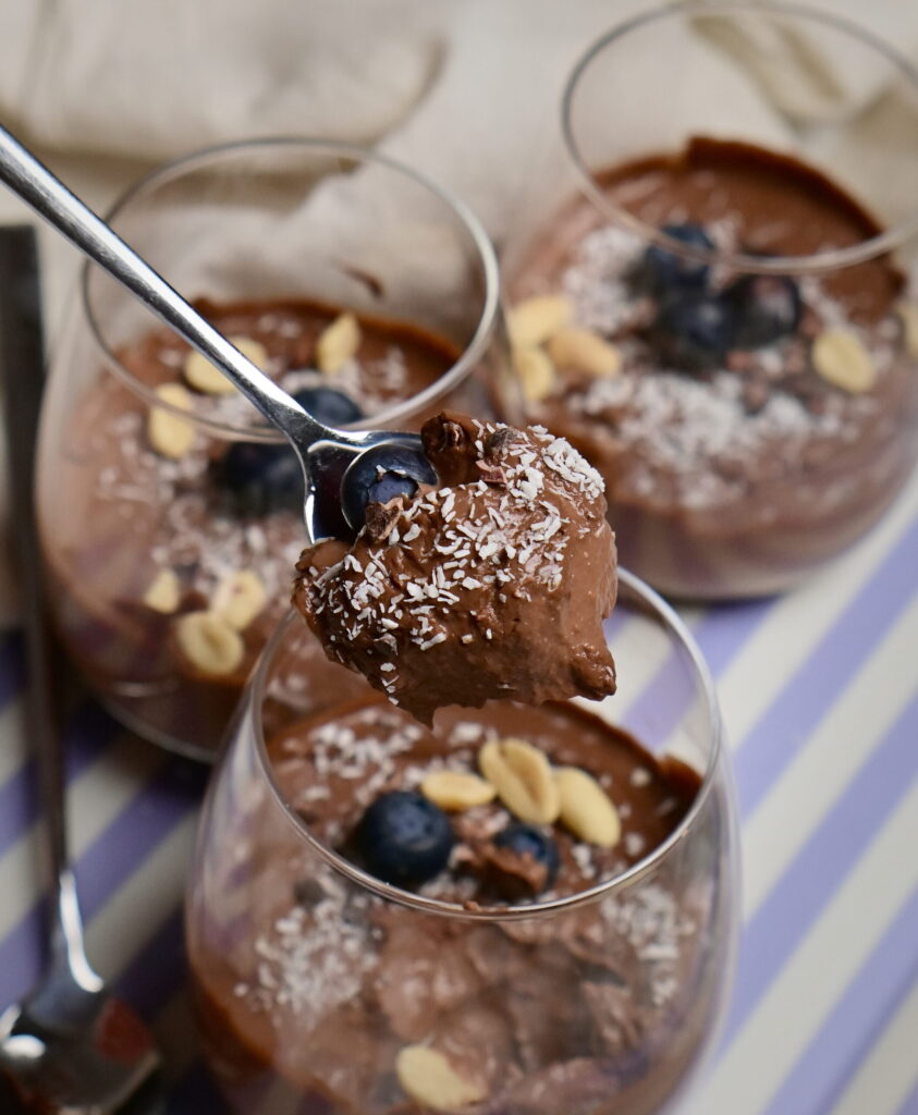 A spoon with chocolate mousse above decorated serving glasses.
