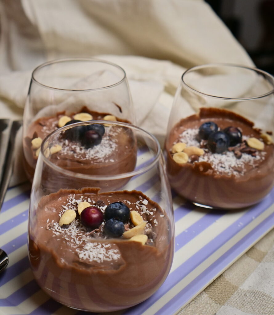Chocolate mousse in serving glasses with coconut, peanuts, and blueberries.