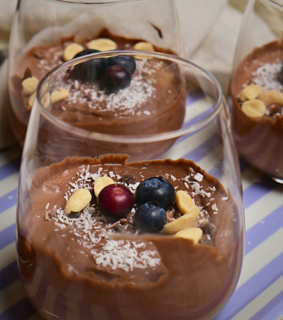 Chocolate mousse in serving glasses with coconut, peanuts, and blueberries.