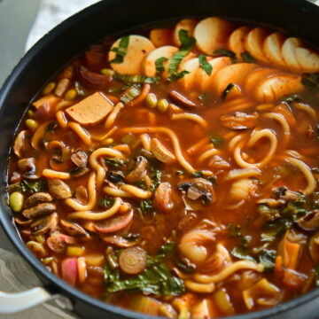 vegan Korean Army Stew (Budae Jjigae) in a shallow pot on a white tablecloth.