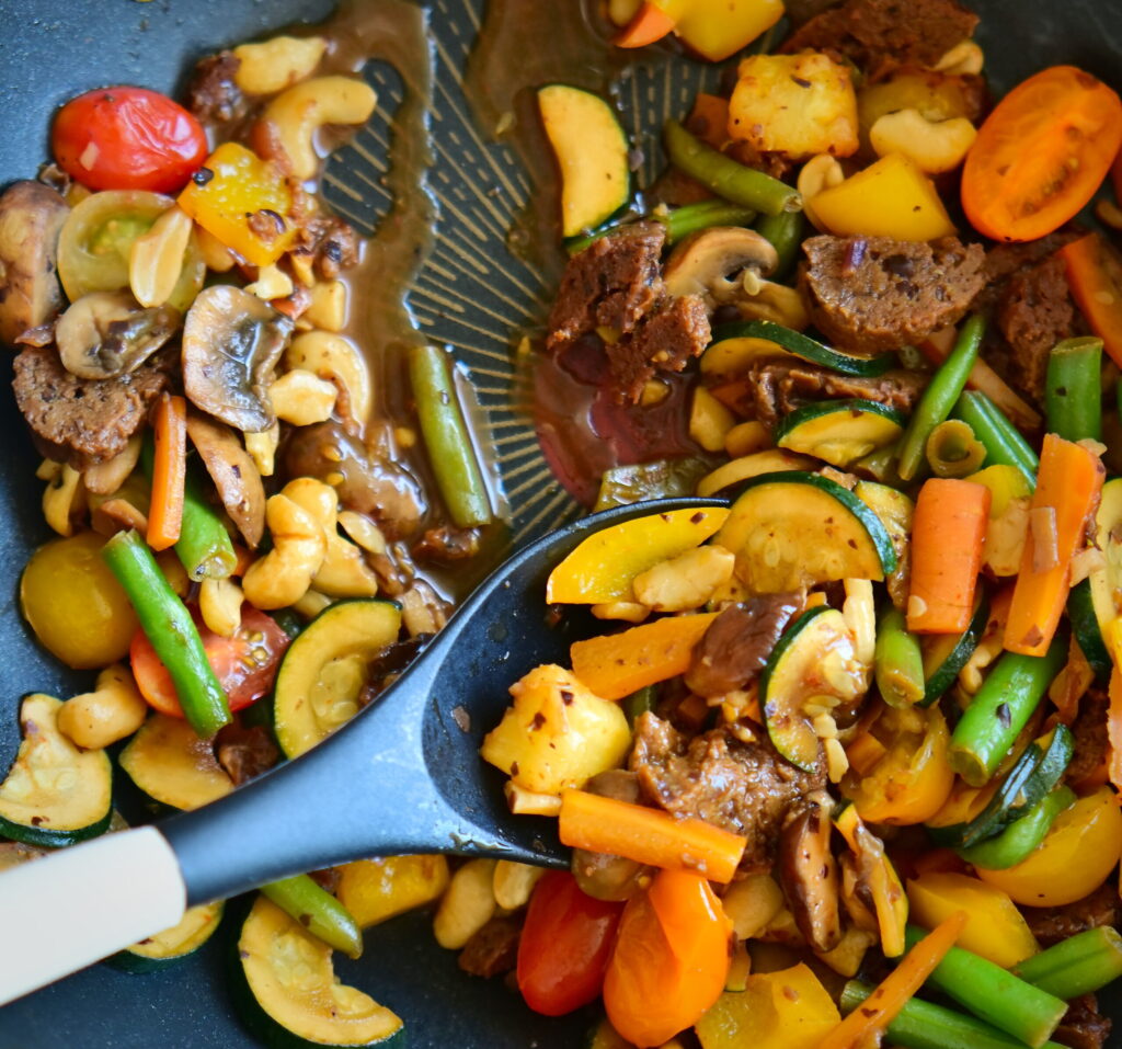 A wok filled with colorful stir-fried vegetables and seitan sausages