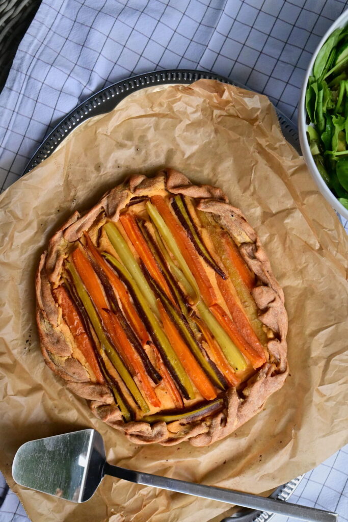 Galette filled with colorful carrots, next to a serving spoon on parchment paper.