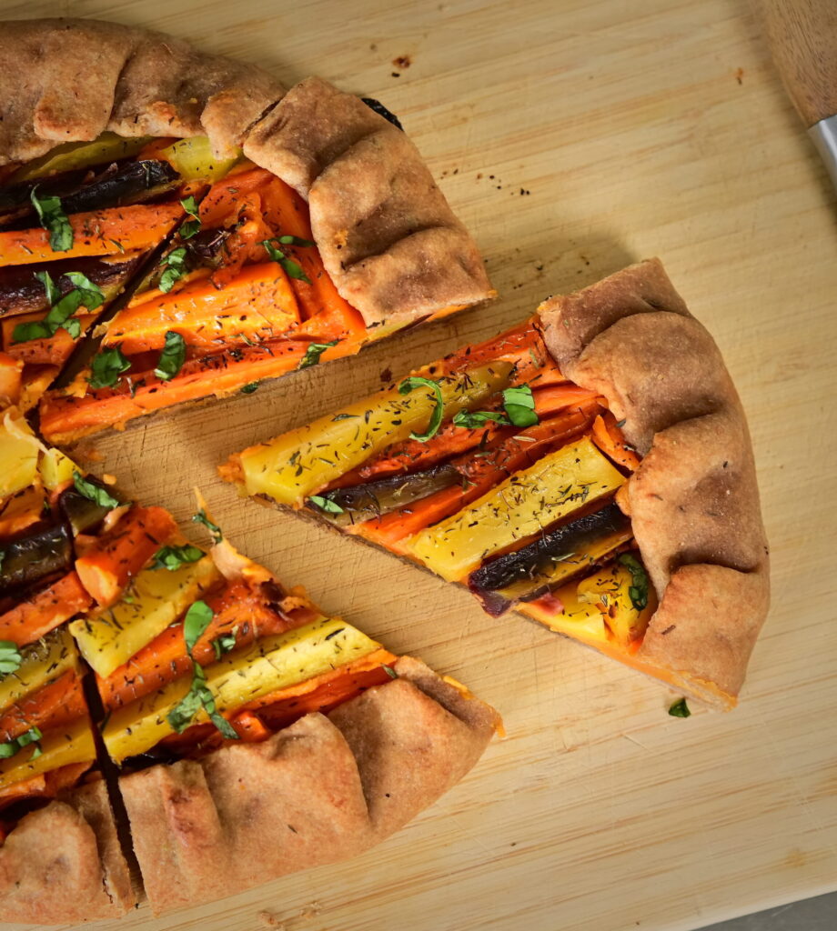 A slice of galette filled with colorful carrots, on a wooden board.