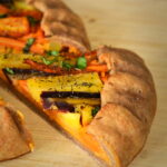 A slice of galette filled with colorful carrots, on a wooden board.
