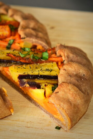 A slice of galette filled with colorful carrots, on a wooden board.