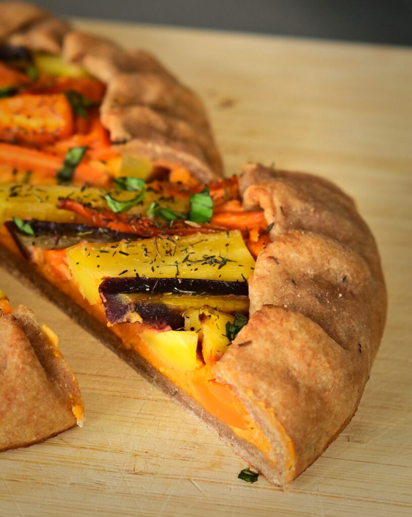 A slice of galette filled with colorful carrots, on a wooden board.