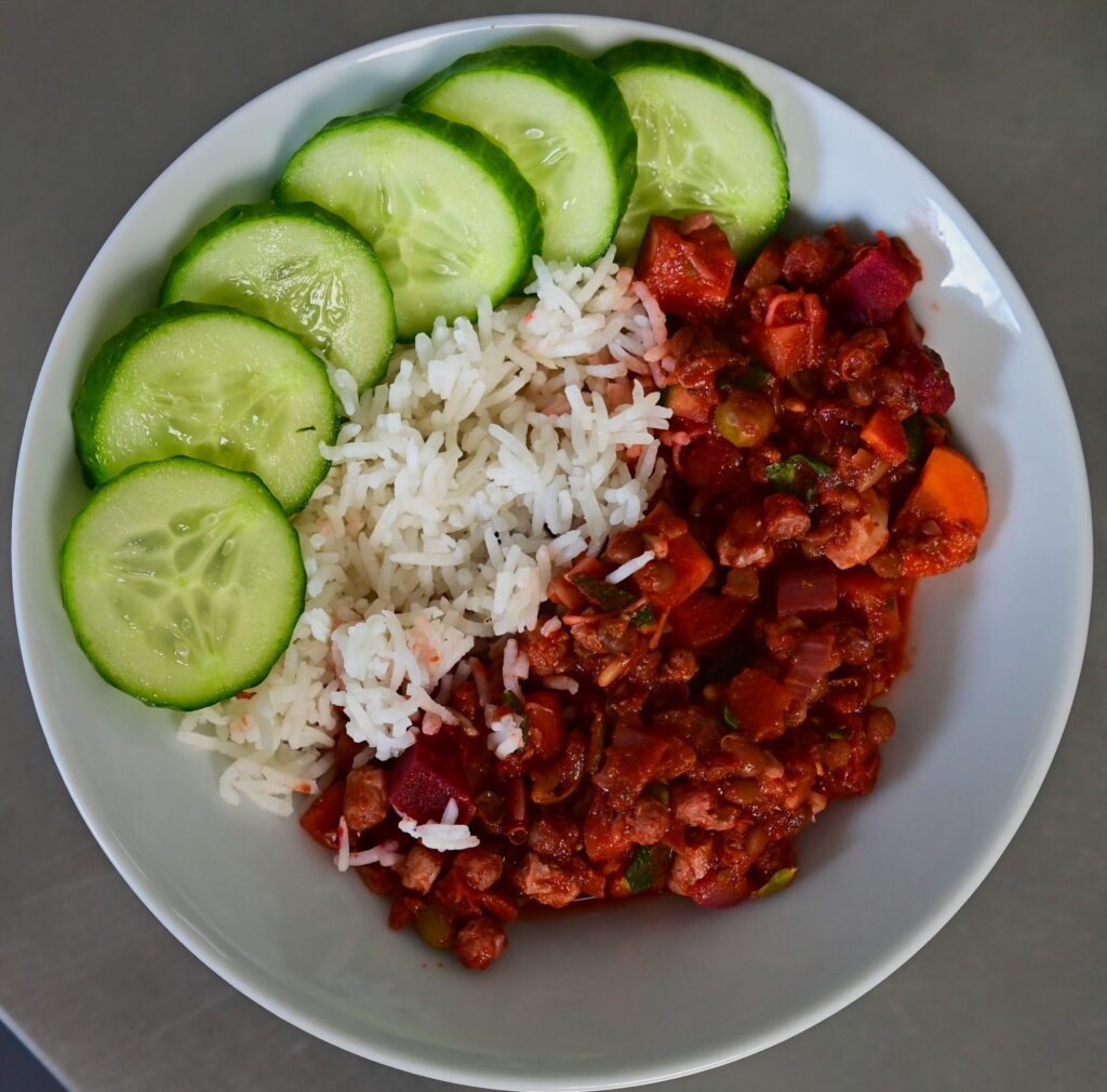 A bowl with Veggie-Packed Vegan Mince, rice and cucumbers